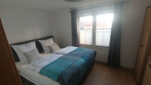 A bedroom with a bed, a window with curtains, a radiator, and a wooden floor. - Cozy, bright apartment in a very quiet location (Detmold)