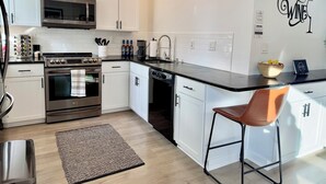 A modern kitchen with white cabinets, stainless steel appliances, a black countertop, and a brown chair. - Downtown Dayton townhouse with private garage AND rooftop patio! (Dayton)