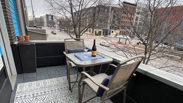 A balcony with a table, chairs, and a bottle of wine. There are potted plants on the windowsill and a patterned rug on the floor. - Downtown Dayton townhouse with private garage AND rooftop patio! (Dayton)