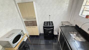 A compact kitchen with a microwave, a small stove, a sink, and a cabinet.