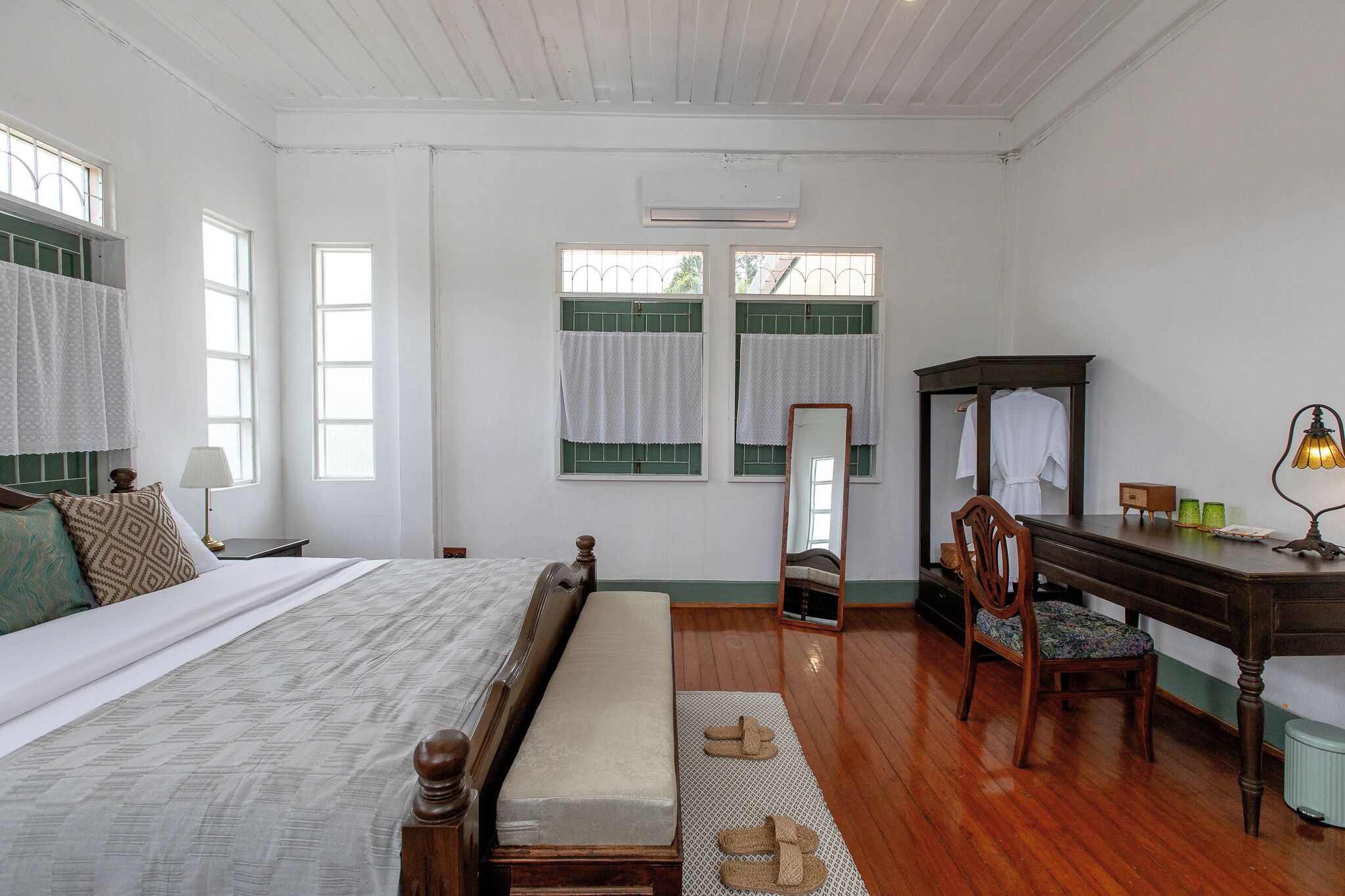 Un dormitorio con cama, un banco, un escritorio con silla, un espejo y una lámpara.