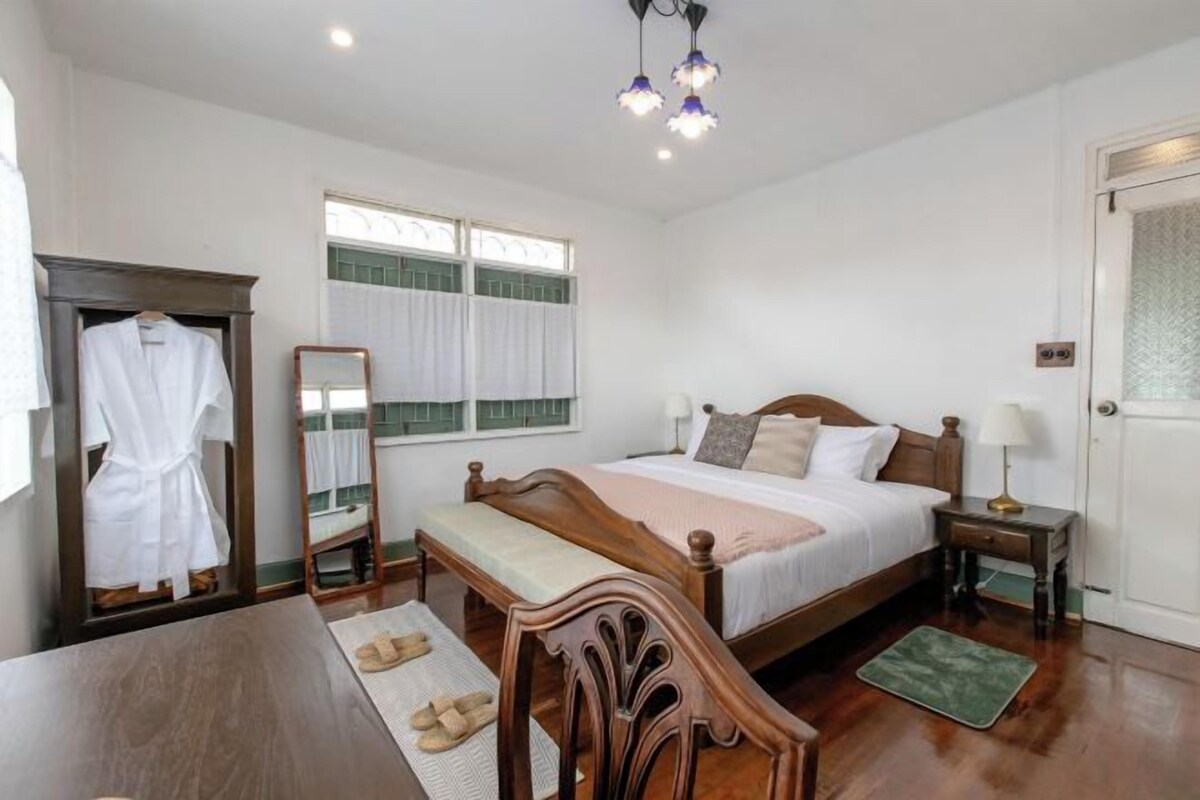 Quarto com cama de madeira, mesas de cabeceira, espelho, roupão e janela com cortinas.