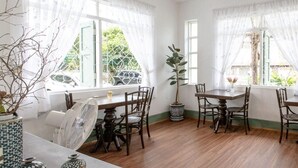 A dining area with a wooden table and chairs, white curtains, and a potted plant.