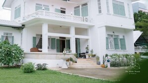A two-story white house with a balcony, a fountain, and potted plants in the garden.