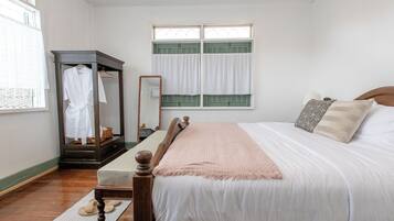 Quarto com cama de madeira, mesa de cabeceira, espelho, guarda-roupa e janela com cortinas.