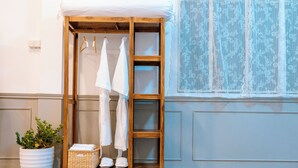 A wooden wardrobe with hanging space and shelves, a potted plant, and a window with lace curtains.