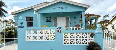 A small, single-story building with a light blue exterior, a white door, and a small balcony.