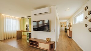A modern living room with a flat-screen TV mounted on the wall, wooden flooring, a built-in entertainment unit, and a kitchen area in the background. - Feel Discovery Casal do Temporão Douro (Peso da Régua)