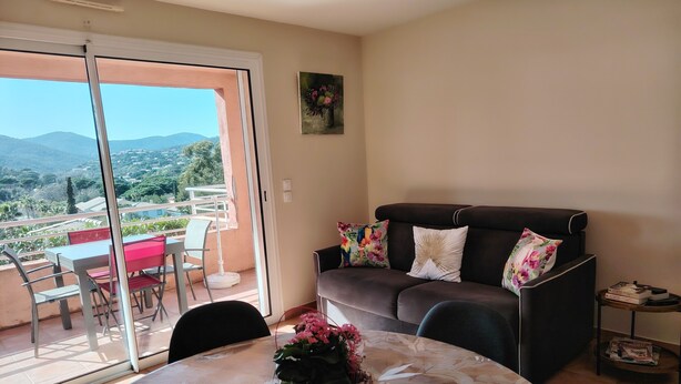 A living room with a sofa, a table with a floral tablecloth, and a potted plant. - Appart. T2 Les Issambres 400 m from beaches and port (Roquebrune-sur-Argens)