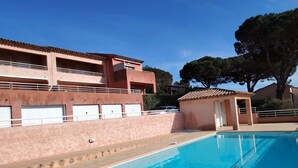 A swimming pool with a tiled deck, a small covered area, and a building with multiple balconies and garage doors. - Appart. T2 Les Issambres 400 m from beaches and port (Roquebrune-sur-Argens)