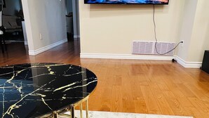 A modern living room with a flat-screen TV mounted on the wall, a black marble table with gold legs, and a patterned rug on the wooden floor. - 3-Bedrooms House in Mississauga with WiFi, AC, Parking. Main floor (Mississauga)