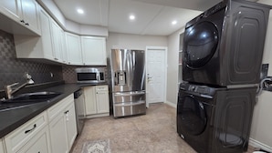 A compact kitchen with white cabinets, a stainless steel refrigerator, a microwave, and a black washing machine. - 3-Bedrooms House in Mississauga with WiFi, AC, Parking. Main floor (Mississauga)