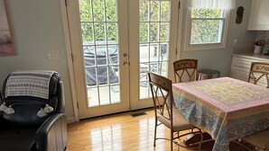 A room with a dining table, chairs, a black leather chair, a small rug, and a window with curtains.
