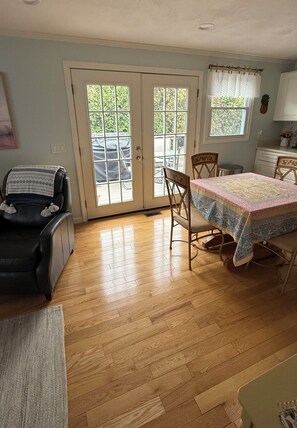 A room with a dining table, chairs, a black leather chair, a small rug, and a window with curtains.