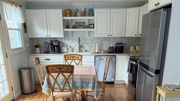 A kitchen with white cabinets, a stainless steel refrigerator, a coffee maker, and a dining table with chairs.