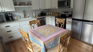 A kitchen with white cabinets, a stainless steel refrigerator, a microwave, and a coffee maker. There is a wooden dining table with chairs.