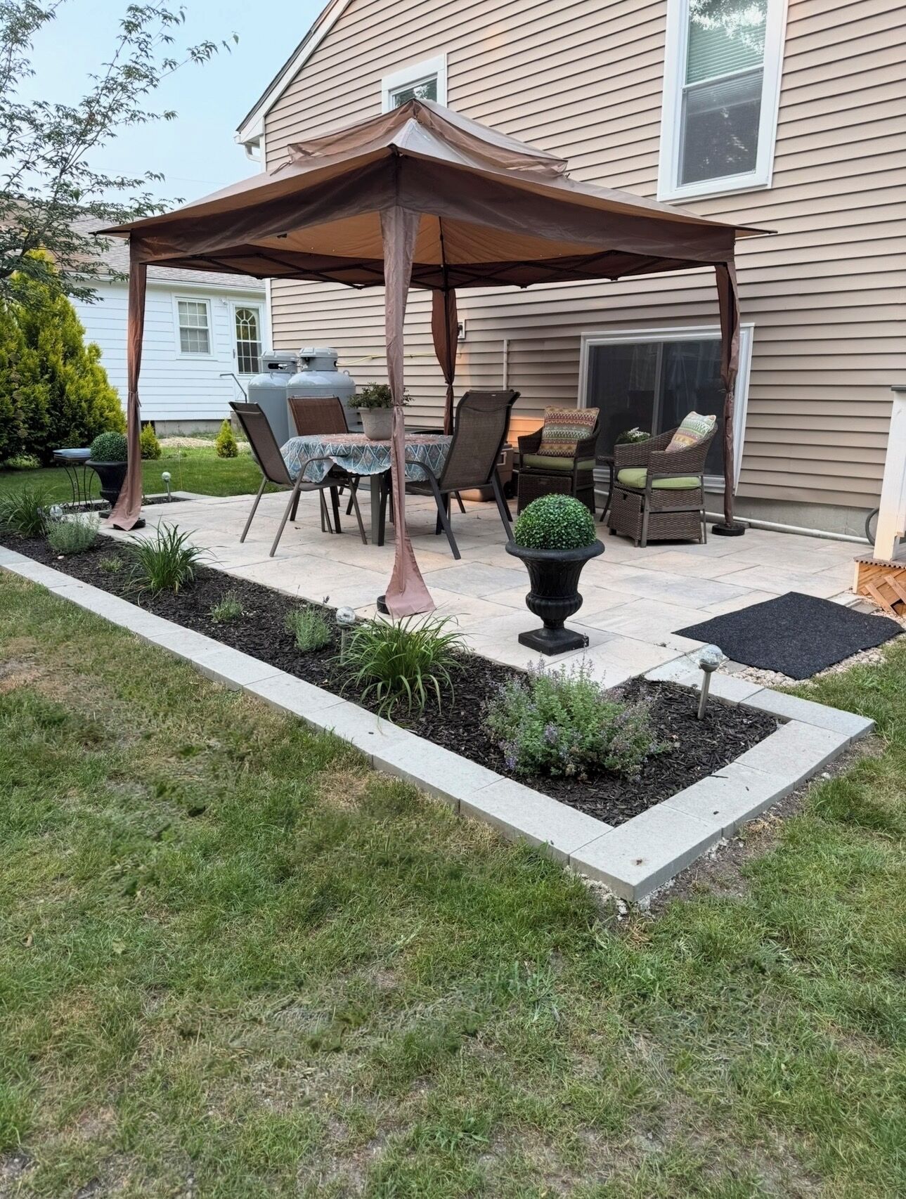 A patio with a covered seating area, outdoor furniture, and a garden bed with plants.