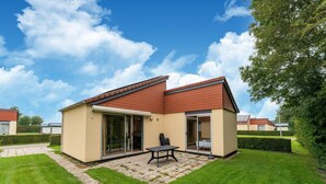 A single-story house with a red roof, a patio with a table and chairs, and a sliding glass door leading to a covered outdoor area. - Holiday Home in Zevenhuizen Near Rottemeren (Zevenhuizen)