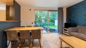 A modern living room with a dining area, a sofa, a TV, and a large sliding glass door leading to a garden. - Holiday Home in Zevenhuizen Near Rottemeren (Zevenhuizen)