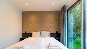A modern bedroom with a large bed, two bedside tables, and a view of greenery through a large window. - Holiday Home in Zevenhuizen Near Rottemeren (Zevenhuizen)
