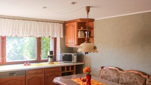 Una cocina con armarios de madera, microondas, cafetera y un comedor con mesa y banco.