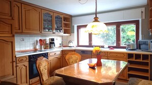 Una cocina con armarios de madera, una mesa de comedor con sillas, una cafetera, un hervidor y una ventana con vistas a la vegetación.