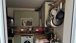 Cocina compacta con lavadora, un taburete de madera y una encimera con utensilios de cocina.