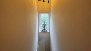 Una escalera estrecha con ventanal en la parte superior, un accesorio de iluminación arriba y barandal blanco.