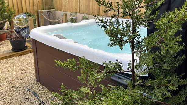 Un jacuzzi rodeado de grava, una valla de madera y una planta en maceta.