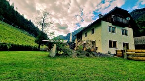 Una casa de dos pisos con un balcón, una piedra en el jardín delantero y montañas al fondo.