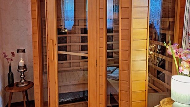 Un gabinete de madera con puertas de vidrio, una estatua encima y una pequeña mesa con una vela y flores a su lado.