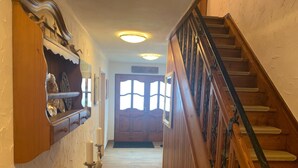 Una escalera de madera con barandilla conduce a una puerta con ventanal. A la izquierda, se observa una estantería adosada con objetos decorativos.