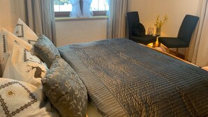 Un dormitorio con cama, dos sillas, una mesita y una ventana con cortinas.