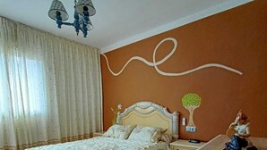A bedroom with a bed, nightstand, dresser, and a wall-mounted lamp.