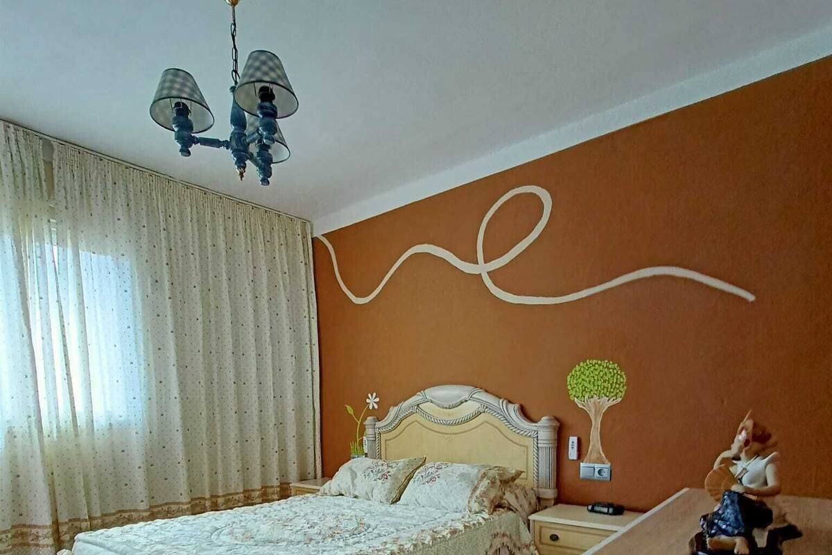 A bedroom with a bed, nightstand, dresser, and a wall-mounted lamp.