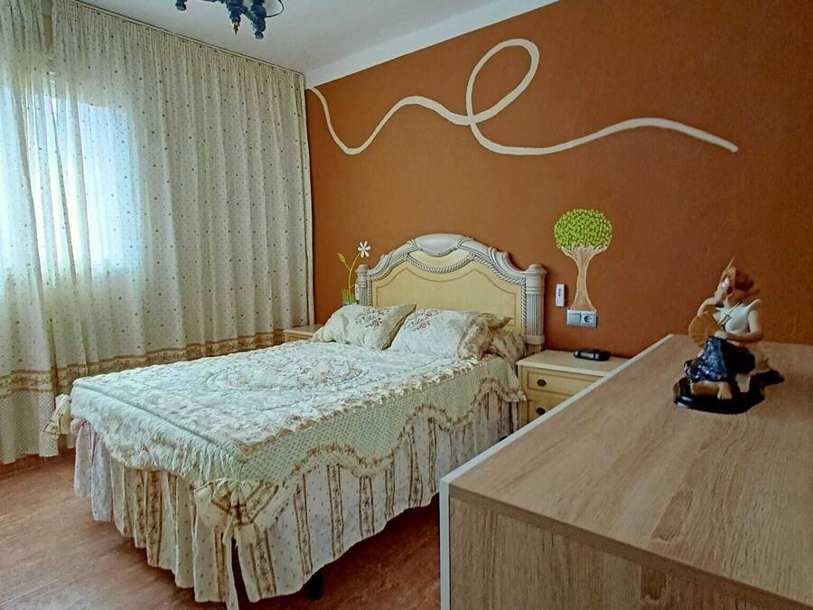 Une chambre à coucher comprenant un lit, une table de chevet, une commode et une lampe fixée au mur.