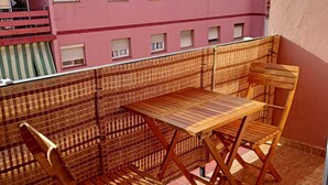 A balcony with a wooden table and chairs, a view of a pink building, and a tiled floor.