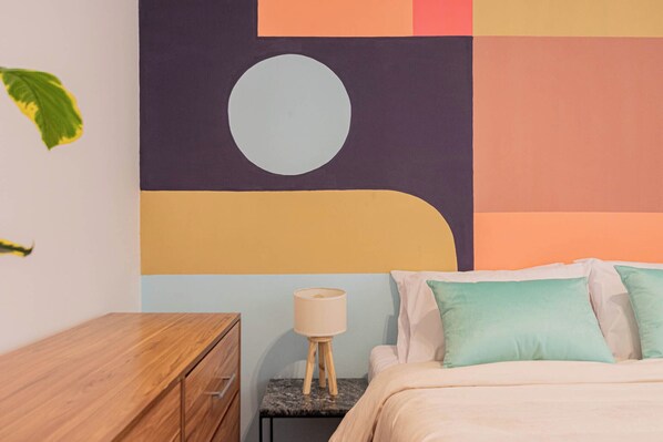 A bedroom with a bed, a nightstand, a lamp, and a wall with abstract art. - MOT + Junin 1200 - 2 Bd en Recoleta (Buenos Aires)