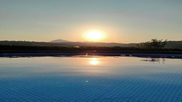 Une piscine offrant une vue dégagée sur le soleil couchant, qui se reflète sur un paysage vallonné.