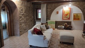 Un salon chaleureux avec un mur en pierre, un canapé blanc, une commode en bois et une cheminée.