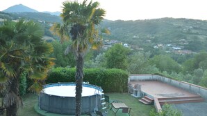 Un jardin avec une piscine ronde, des palmiers et une vue sur une ville et des montagnes en arrière-plan.