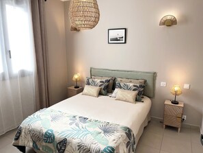 A neatly arranged bedroom with a bed, two bedside tables, a hanging light fixture, and a framed picture on the wall. - Charming one-bedroom apartment with a balcony (Propriano)