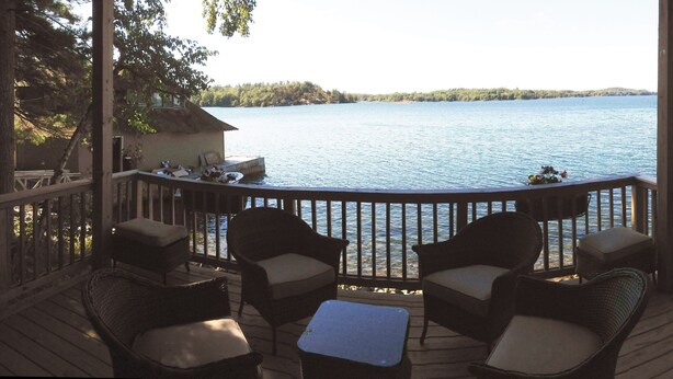A wooden deck with wicker furniture overlooking a lake.