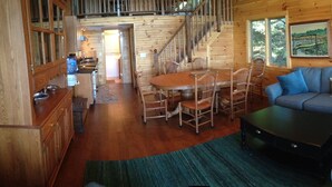 A wooden cabin interior with a dining area, sofa, and staircase.
