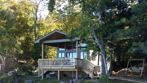 A cabin with a deck overlooking a body of water, surrounded by trees.