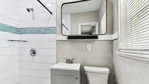 Un baño con azulejos blancos, un lavabo, un inodoro y una ducha.
