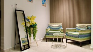 Quarto com duas poltronas, uma mesa redonda pequena, um espelho e uma planta com flores amarelas.