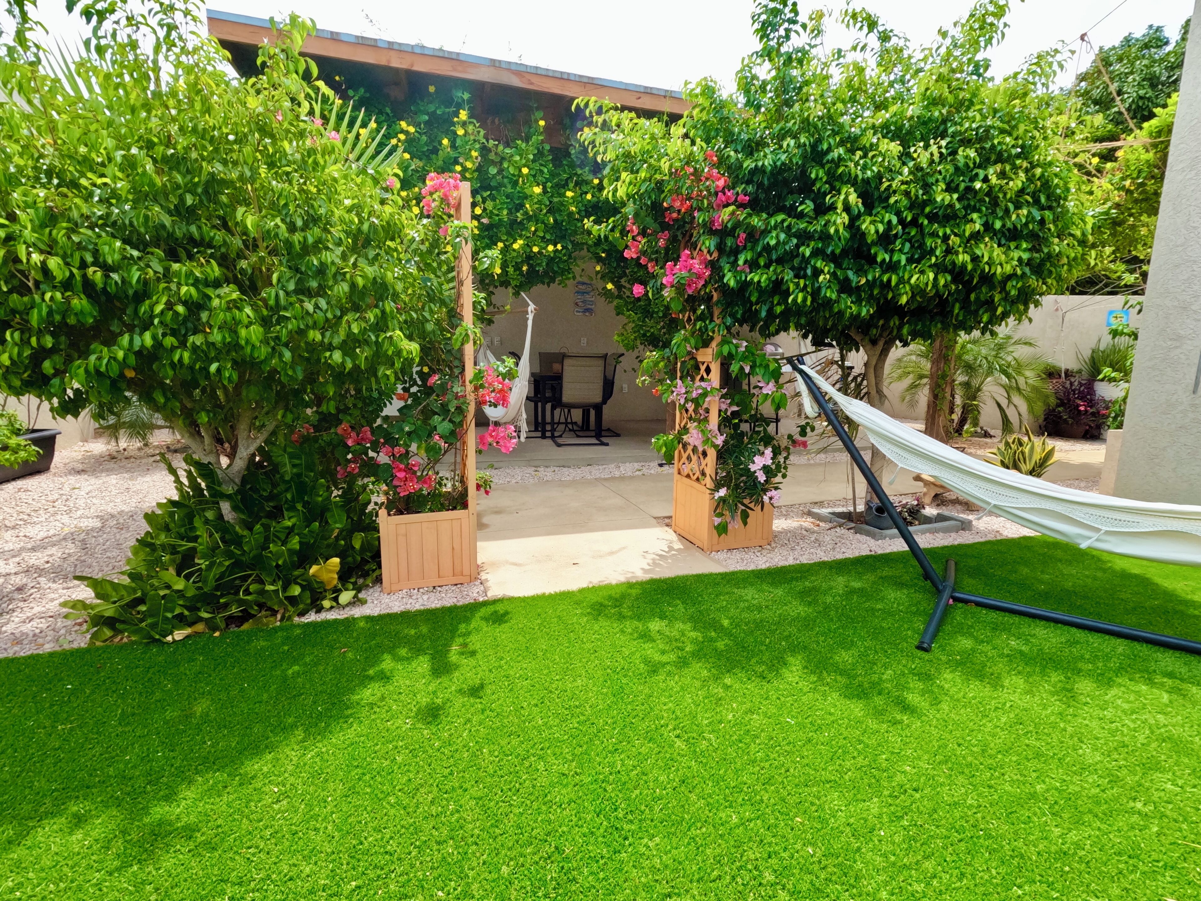 A well-maintained garden with a hammock, a wooden pergola, and a patio area.