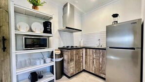 Uma cozinha moderna com armários brancos, micro-ondas embutido, geladeira de aço inoxidável e uma ilha de madeira com pia.