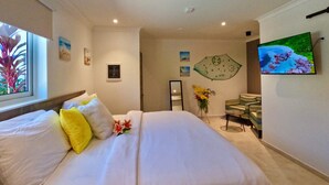 Quarto de hotel com uma cama grande, televisão, escrivaninha e cadeira.